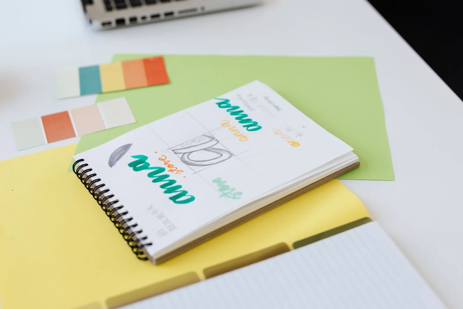 Cuaderno con bocetos de identidad visual y muestras de color sobre una mesa de trabajo.